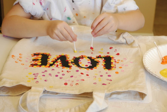 Dieťa maľuje na plátennú tašku pomocou paličiek bodky.